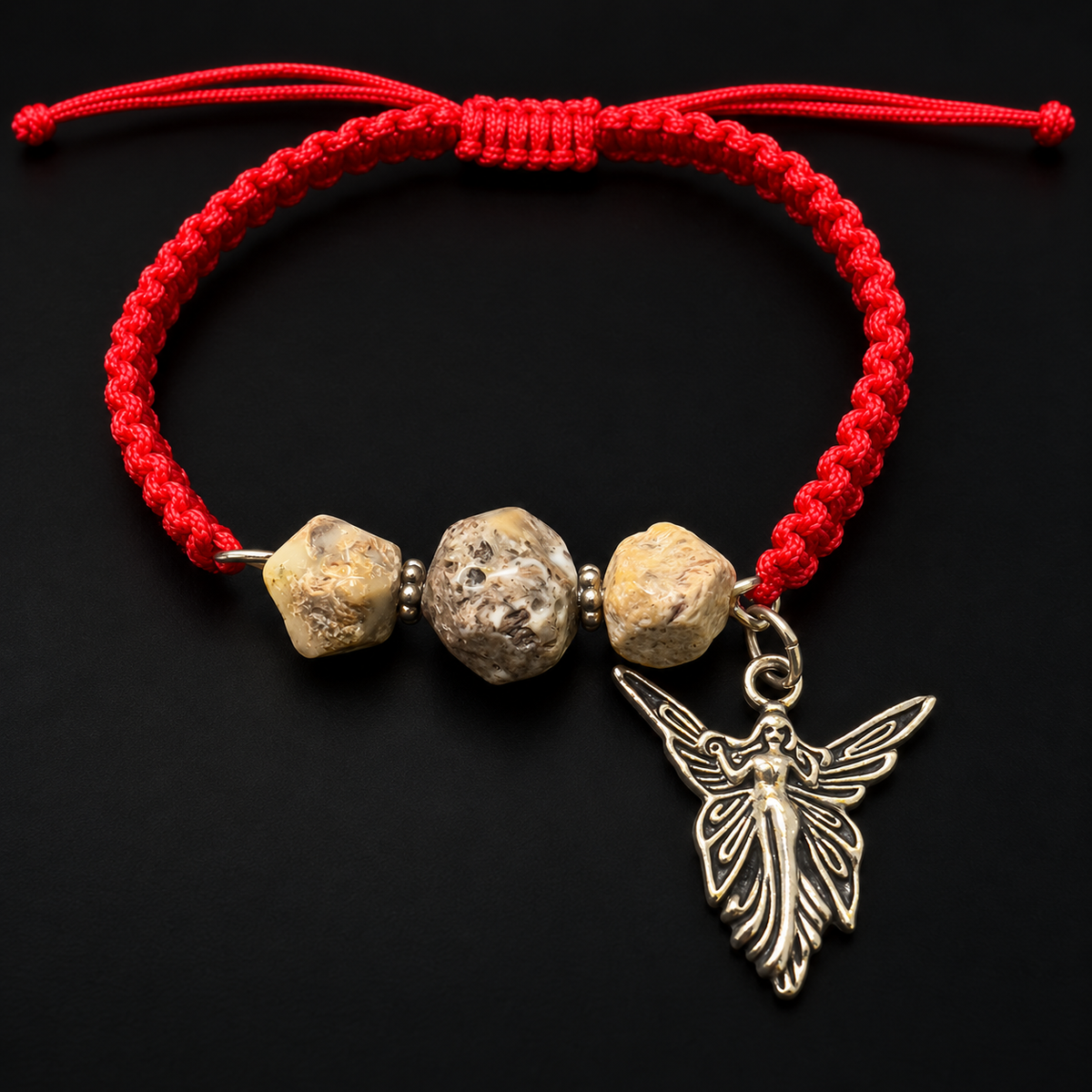 KIZIMA red macrame bracelet with three earthy amber stones and a silver-colored angel charm in black studio lighting.