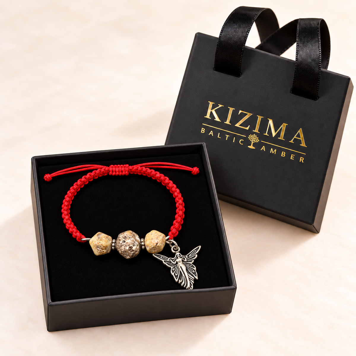 Red macrame earthy amber angel bracelet in a clean black velvet-lined KIZIMA gift box beside its handled gold-logo lid.