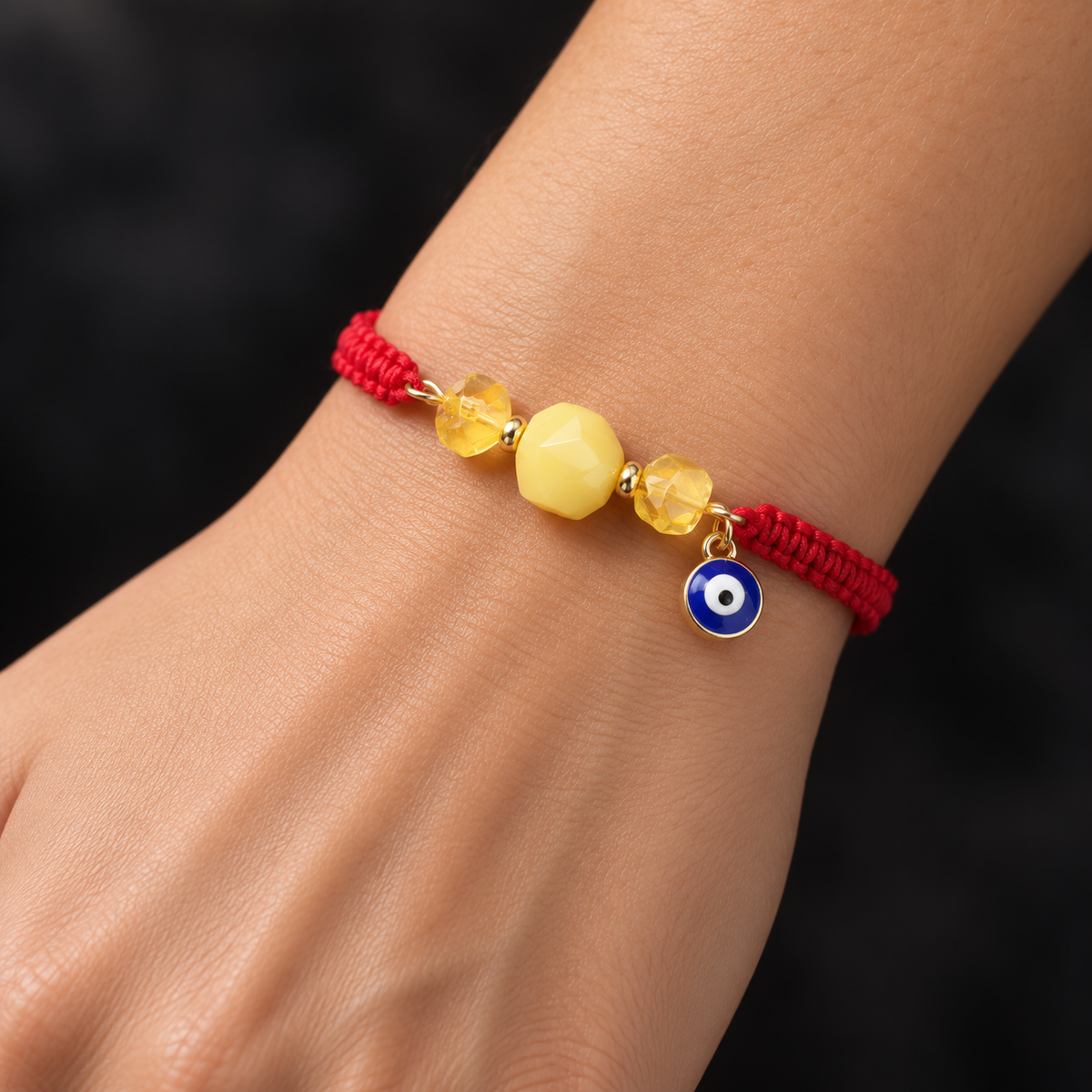 KIZIMA 3G0125q2.81-7 three-bead yellow and honey amber red macrame bracelet with blue evil-eye charm worn on an adult woman's wrist
