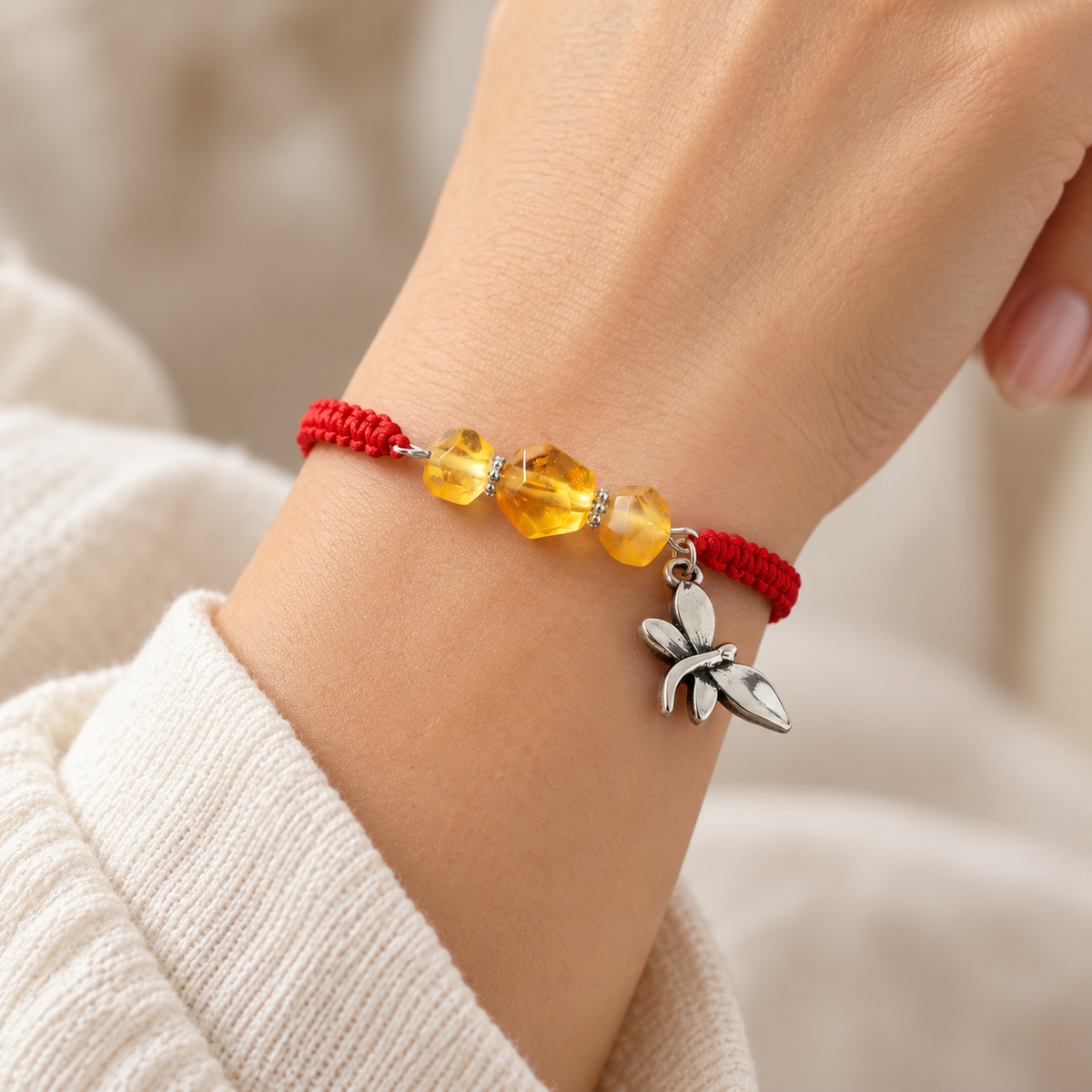 Transparent golden amber beads and a silver-tone dragonfly on a red macrame bracelet worn on a woman's wrist