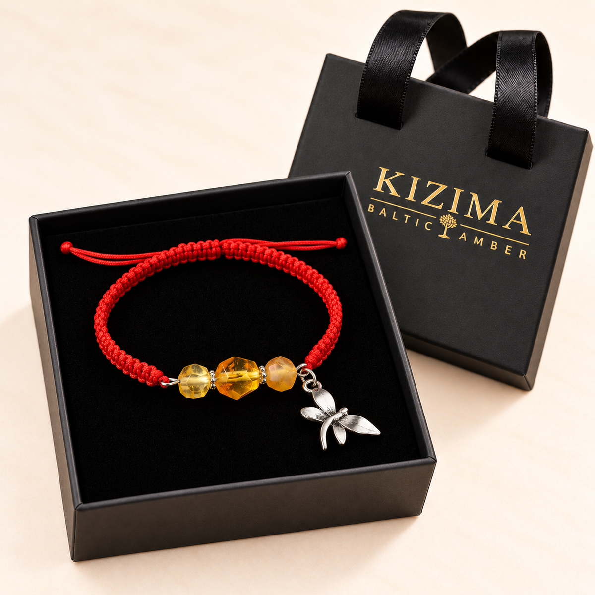 Golden amber and red cord dragonfly bracelet displayed on clean black velvet in a KIZIMA gift box