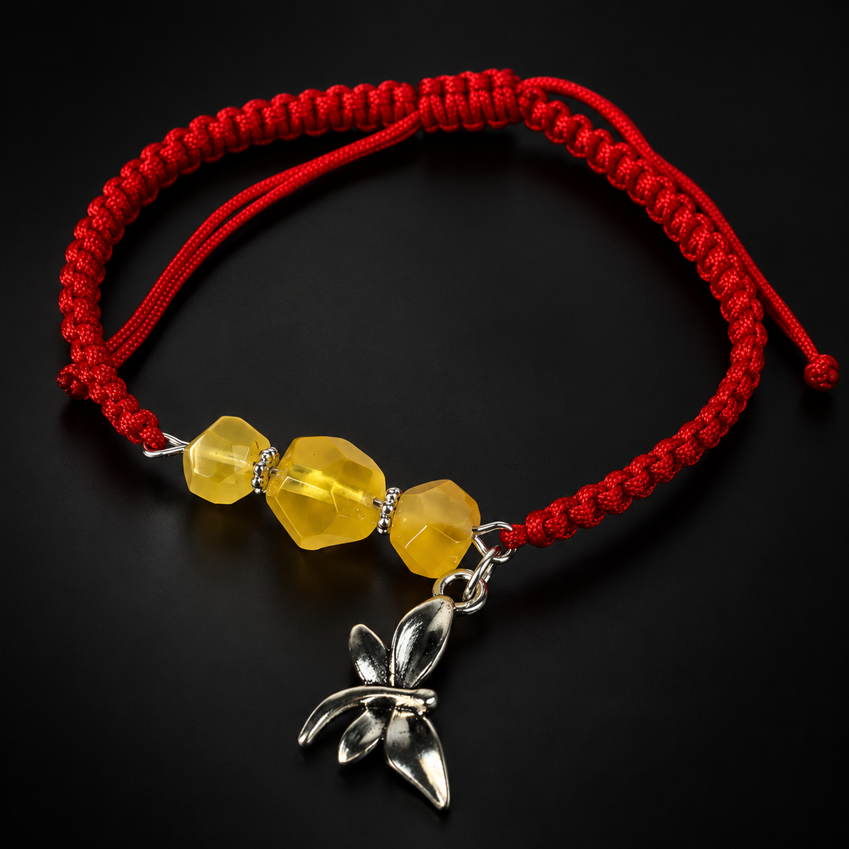 KIZIMA red macrame bracelet with three faceted yellow amber beads and a silver dragonfly charm on a black studio background.