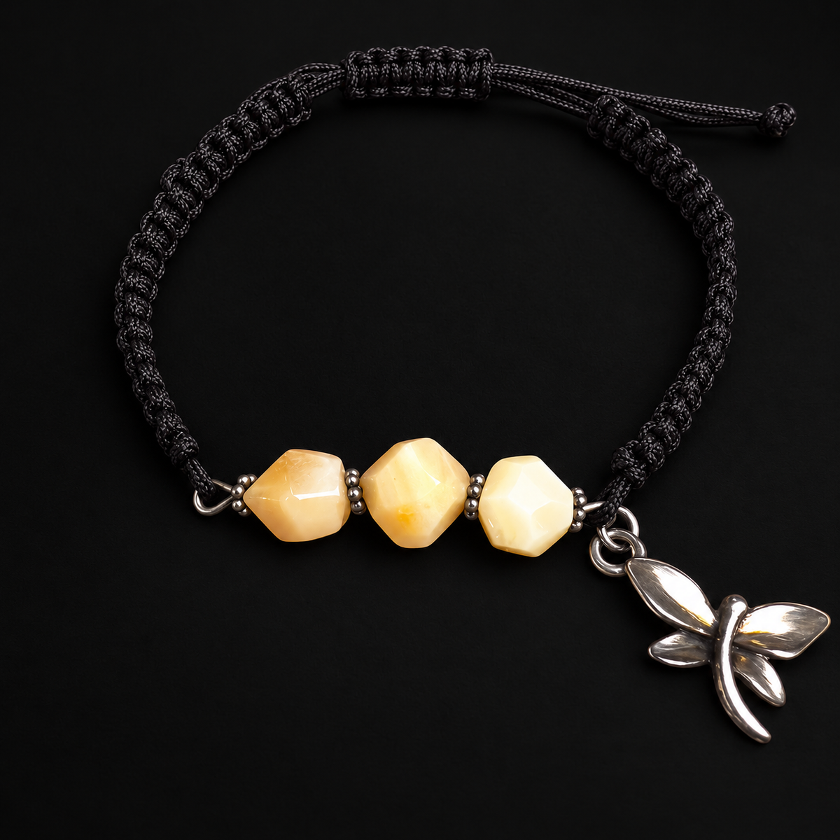 KIZIMA three cream amber stones and silver-tone dragonfly charm on black macrame bracelet in a black studio