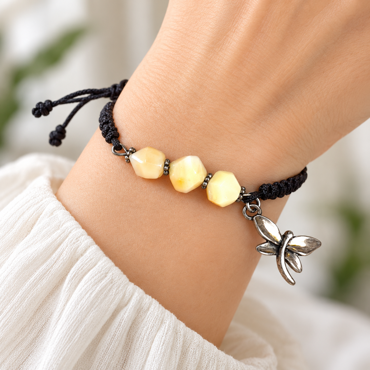 KIZIMA three cream amber stones and silver-tone dragonfly charm on black macrame bracelet on a young adult woman's wrist