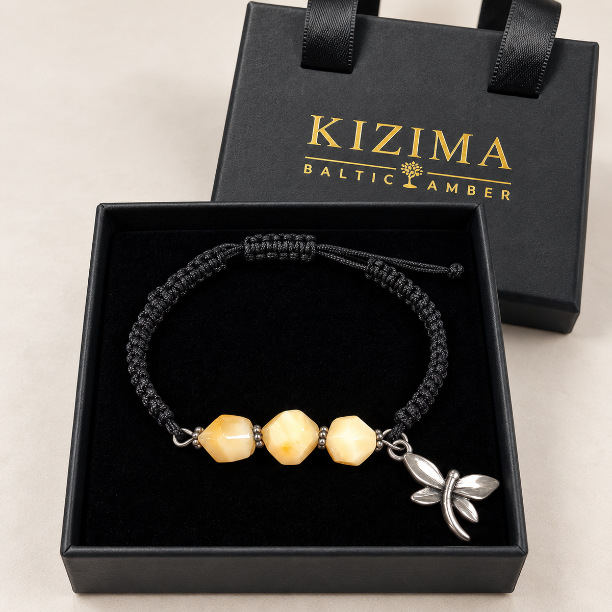 KIZIMA three cream amber stones and silver-tone dragonfly charm on black macrame bracelet inside a black KIZIMA gift box