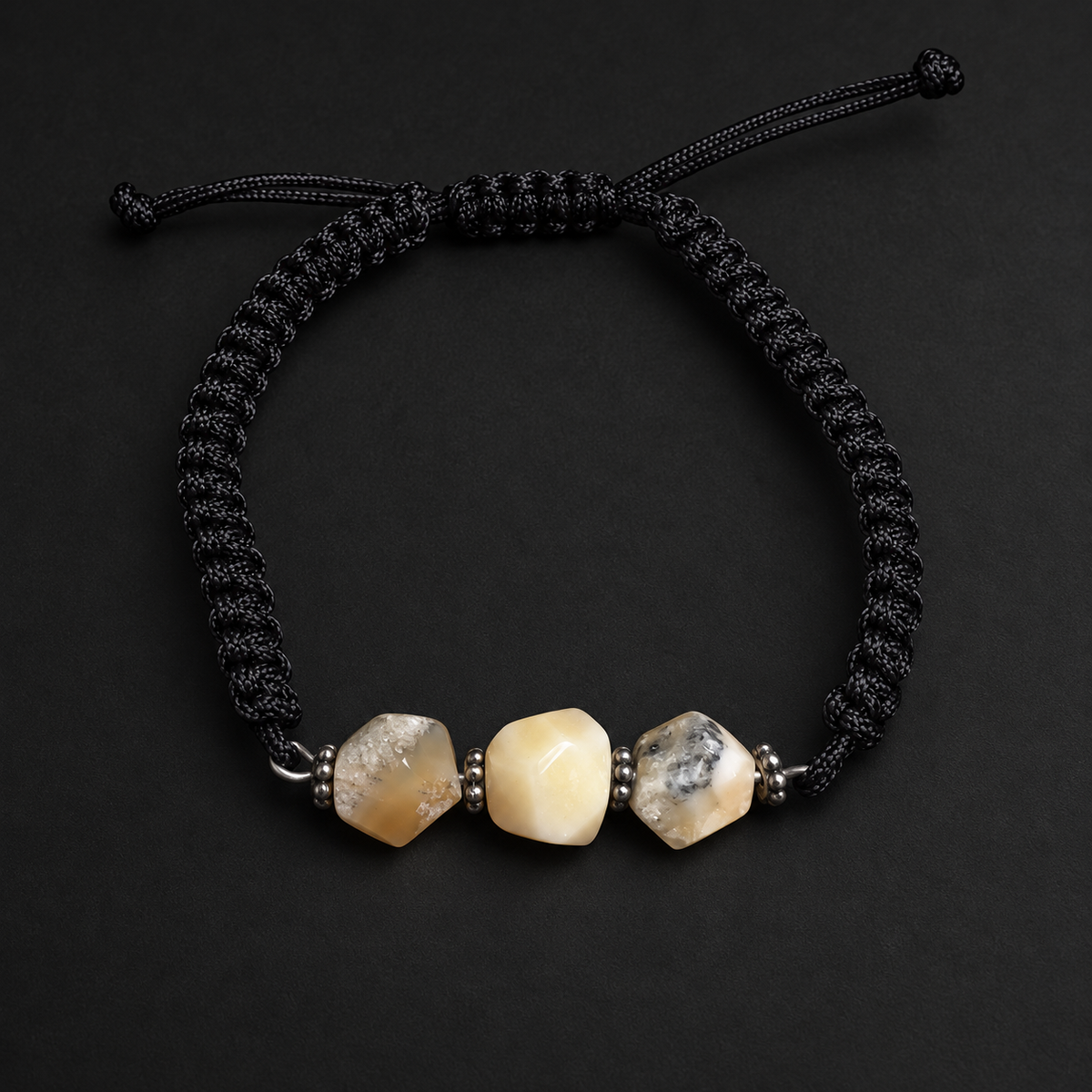 KIZIMA three-stone cream and gray-included amber bracelet on black macrame on a black studio background
