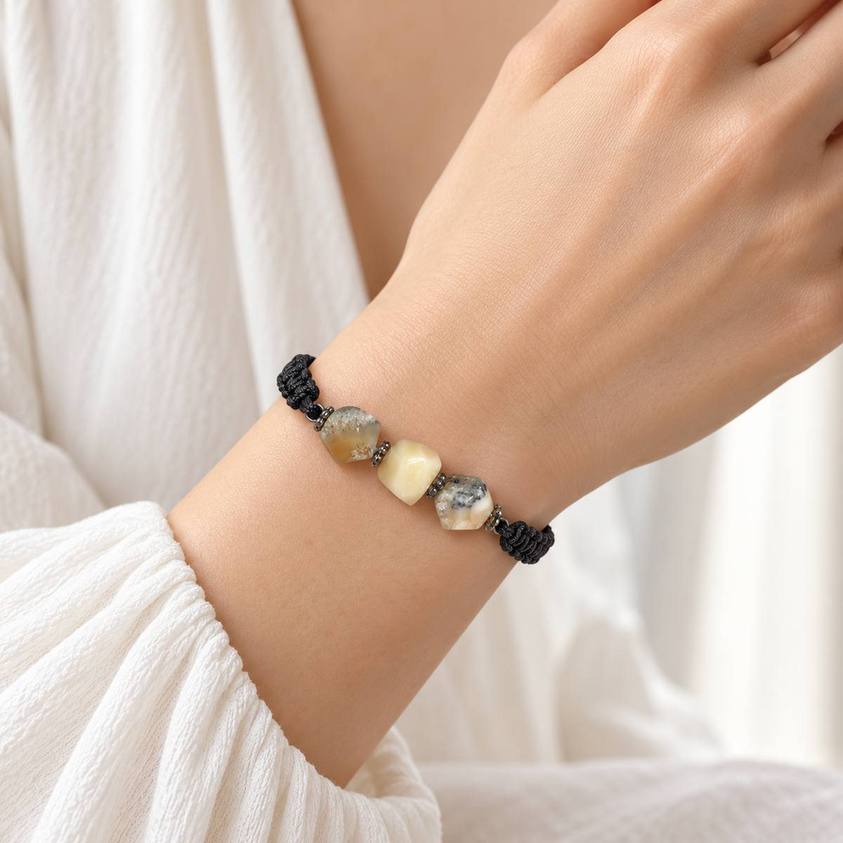 KIZIMA three-stone cream and gray-included amber bracelet on black macrame on a young adult woman's wrist