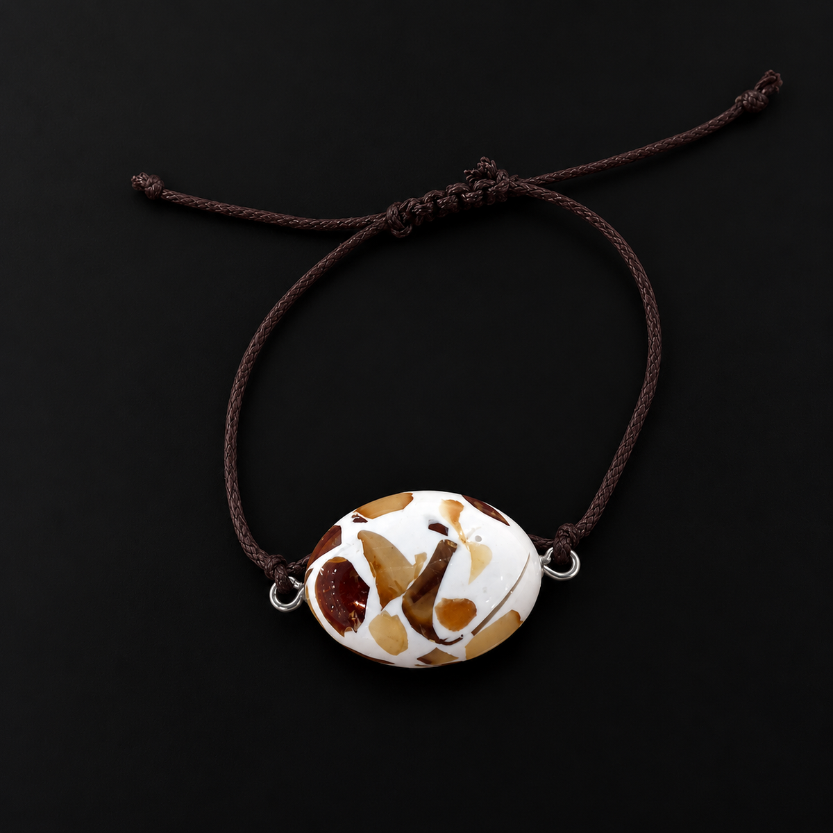KIZIMA 3G0125q3.30 oval white-and-amber mosaic bracelet with dark cord on a black studio surface
