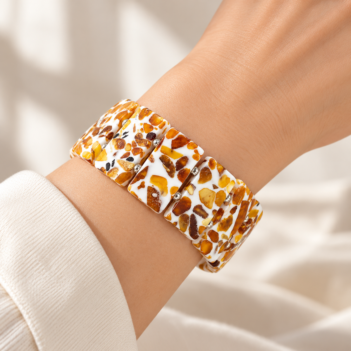 KIZIMA wide white and amber mosaic bracelet with paired silver-colored spacers worn on a young adult woman's wrist