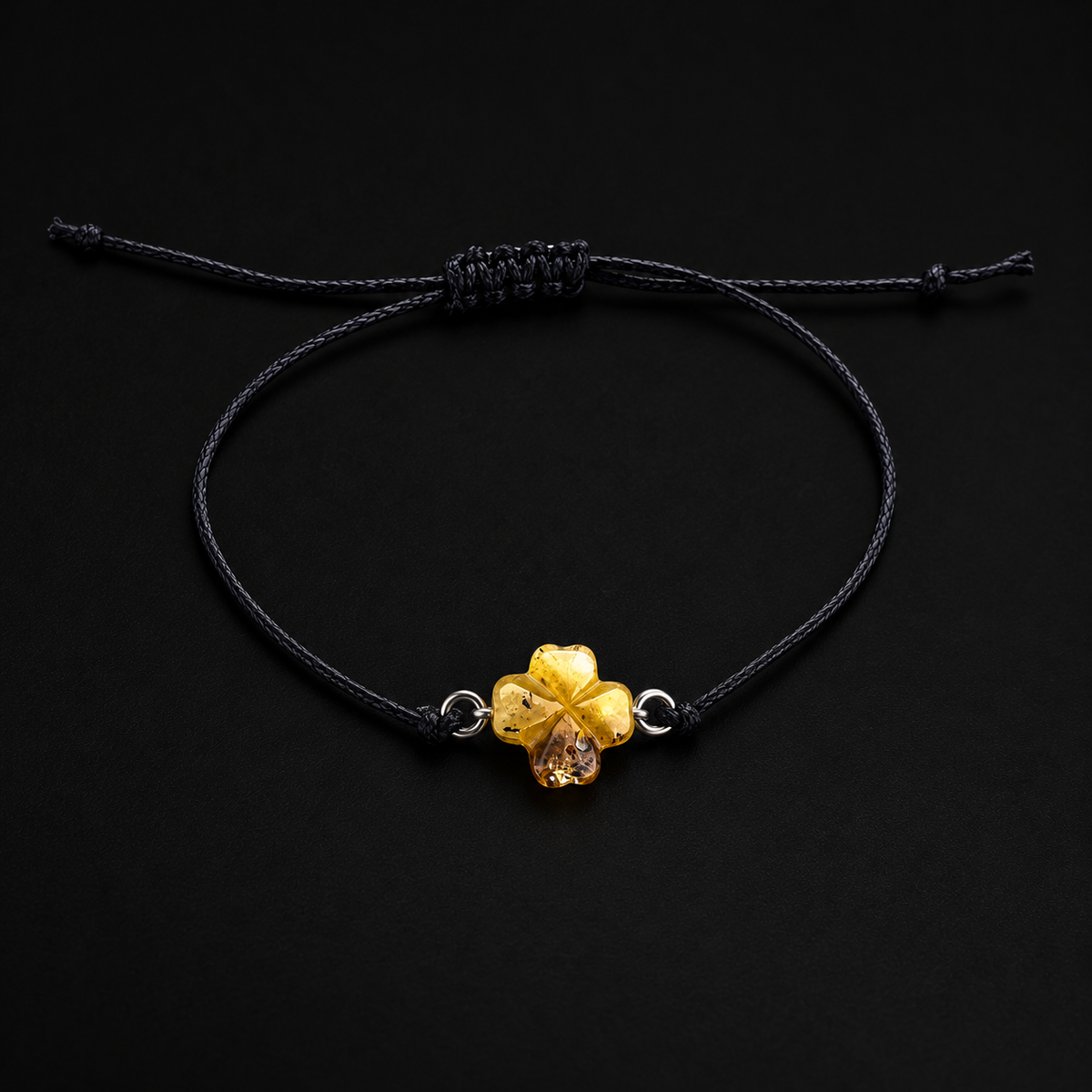 KIZIMA four-leaf clover amber bracelet with black adjustable cord under black studio lighting