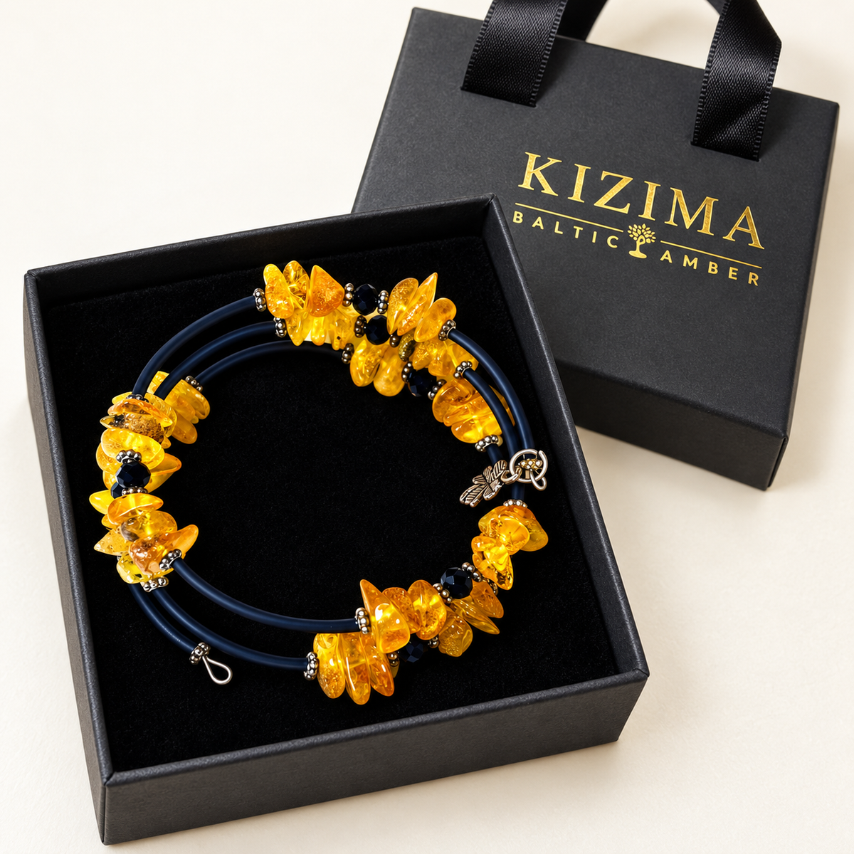 KIZIMA 3G250q16 three-coil spiral bracelet with yellow amber, dark navy sections and black faceted beads on clean black velvet in its KIZIMA gift box