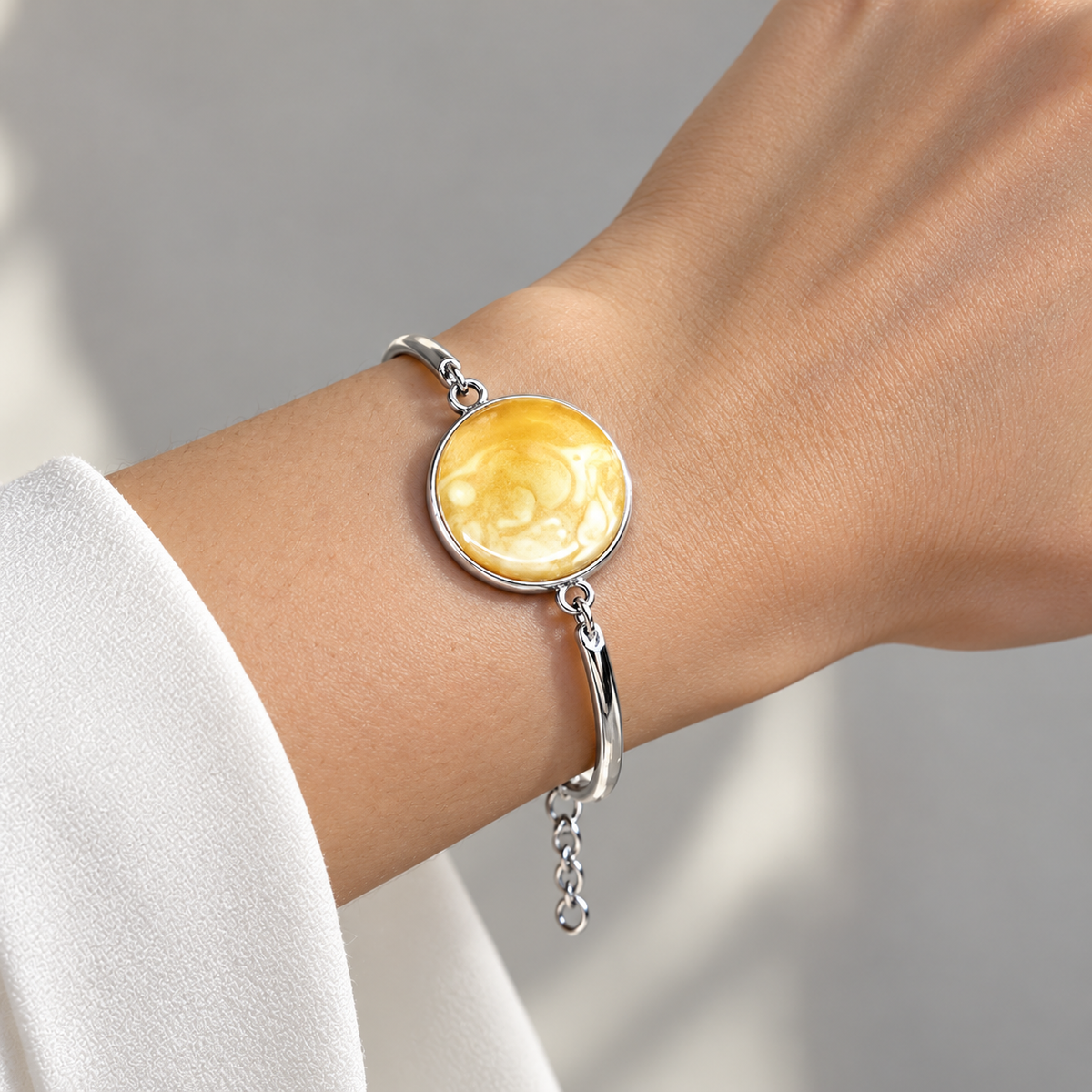 KIZIMA round marbled yellow amber cabochon in silver-tone semi-rigid bracelet on a young adult woman's wrist