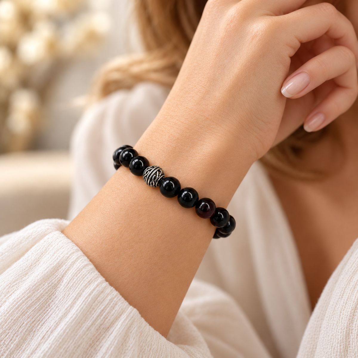 Black amber bracelet worn on a woman's wrist, showing polished round beads and the textured silver-tone accent.