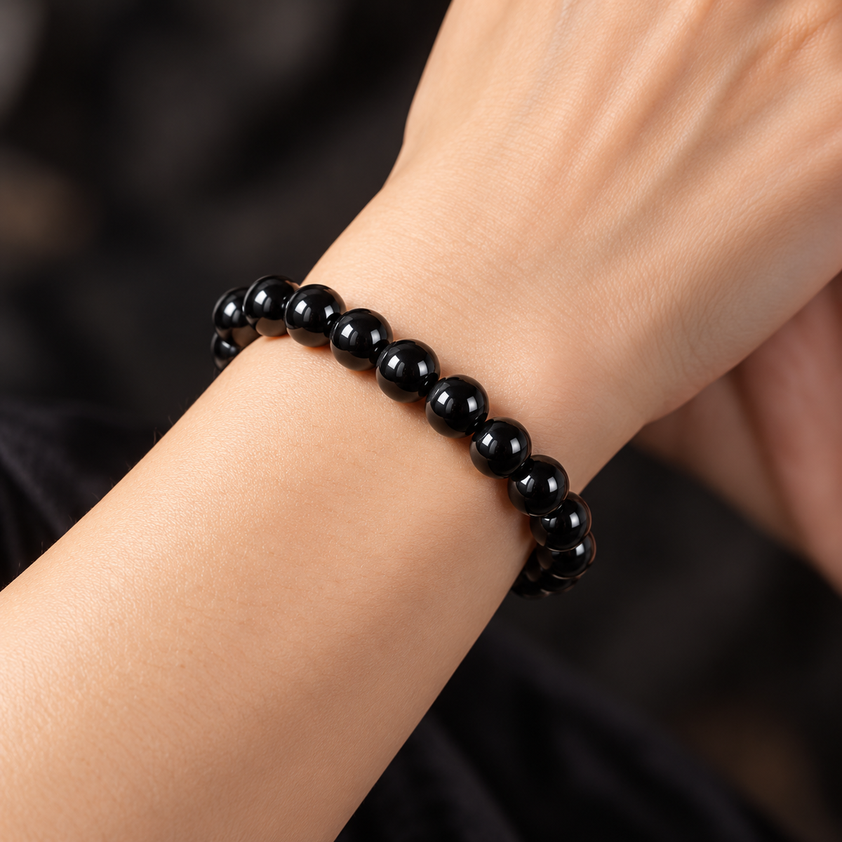 KIZIMA 3KZ0390q13.1 nineteen-bead black amber elastic bracelet worn on an adult woman's wrist