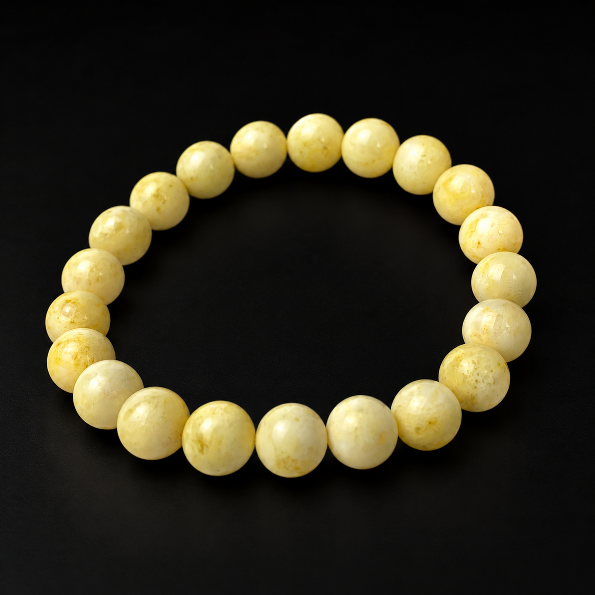 KIZIMA white Baltic amber round-bead bracelet photographed on a matte black studio background.