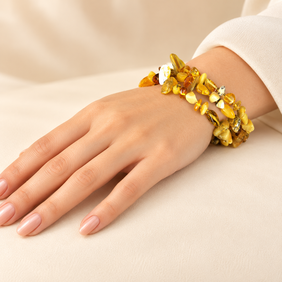 Three-loop amber chip bracelet worn on a young adult woman's hand with a nude manicure.