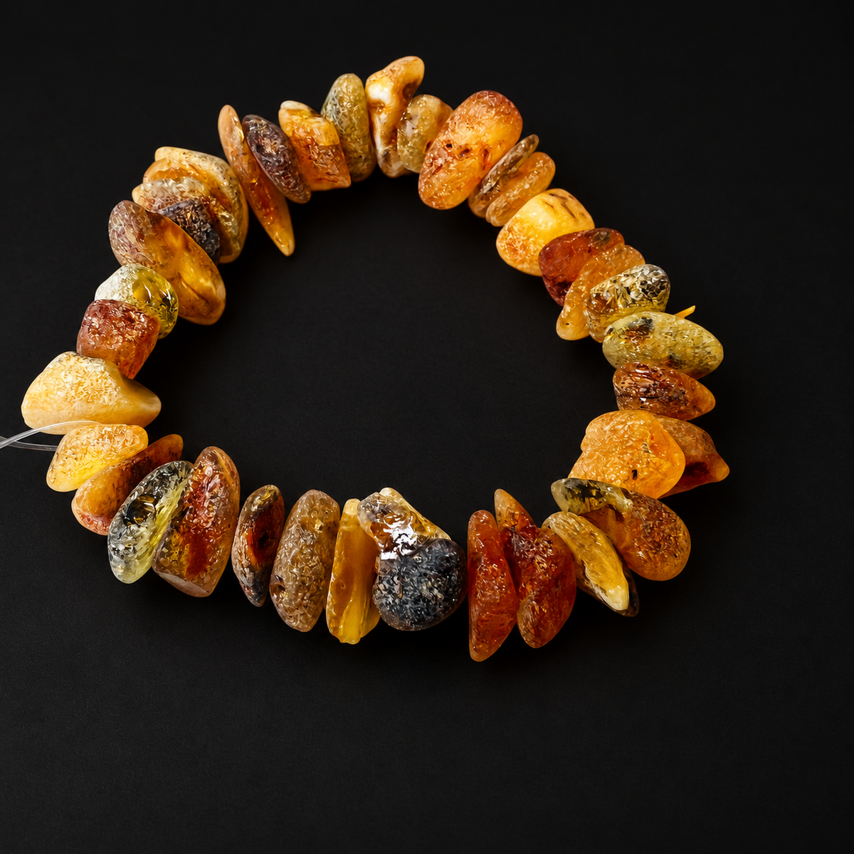 KIZIMA 3N0150q17.16 natural amber chip bracelet with varied honey and mottled tones on a black studio surface