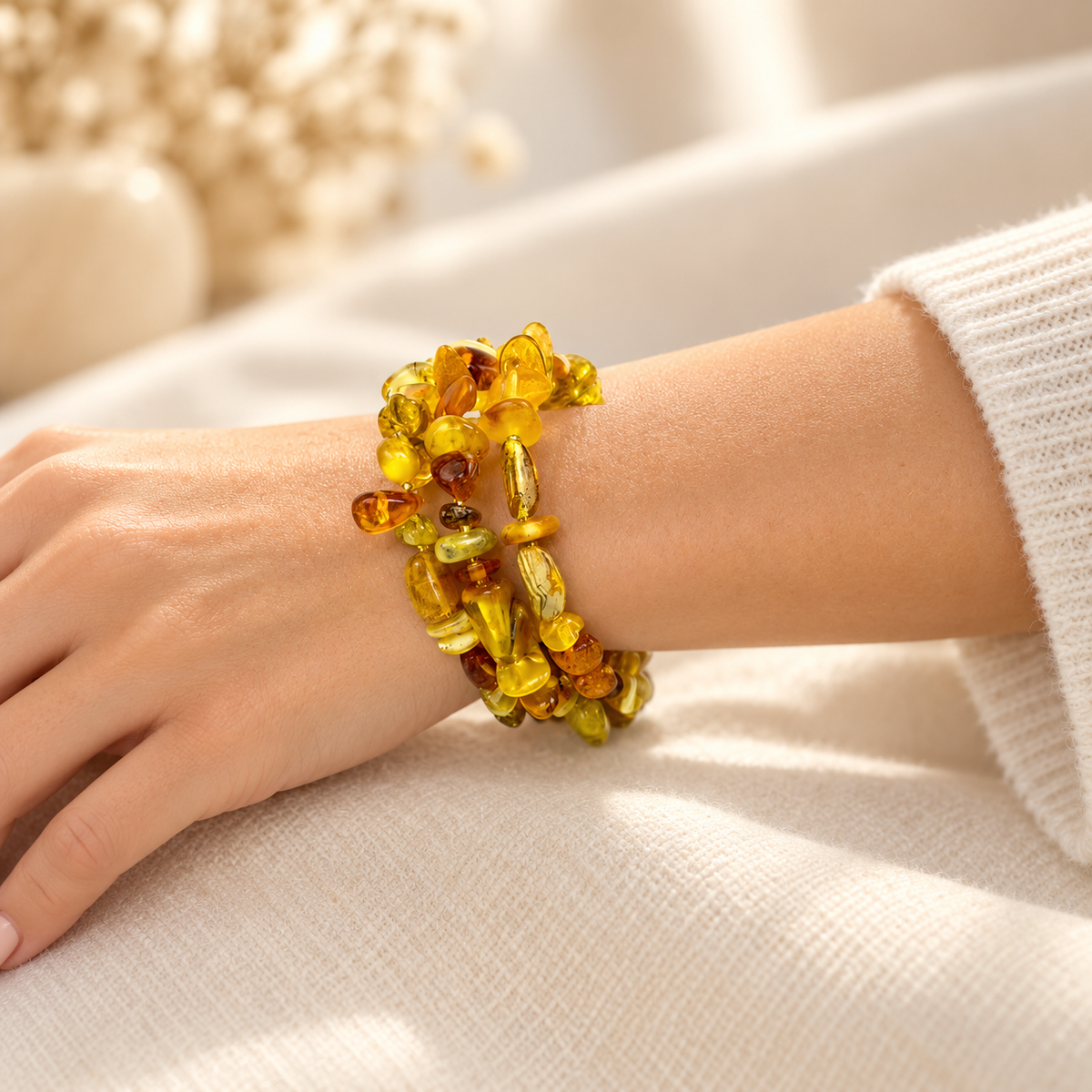 Multicolor Baltic amber spiral bracelet on a young adult woman's wrist beside an ivory sleeve.
