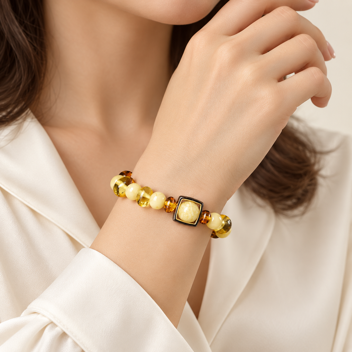 Cream and transparent amber bead bracelet with square-framed centerpiece on an adult woman's wrist.