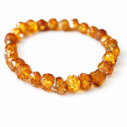 Rough amber nuggets in honey and cognac tones arranged as a bracelet on pure white.