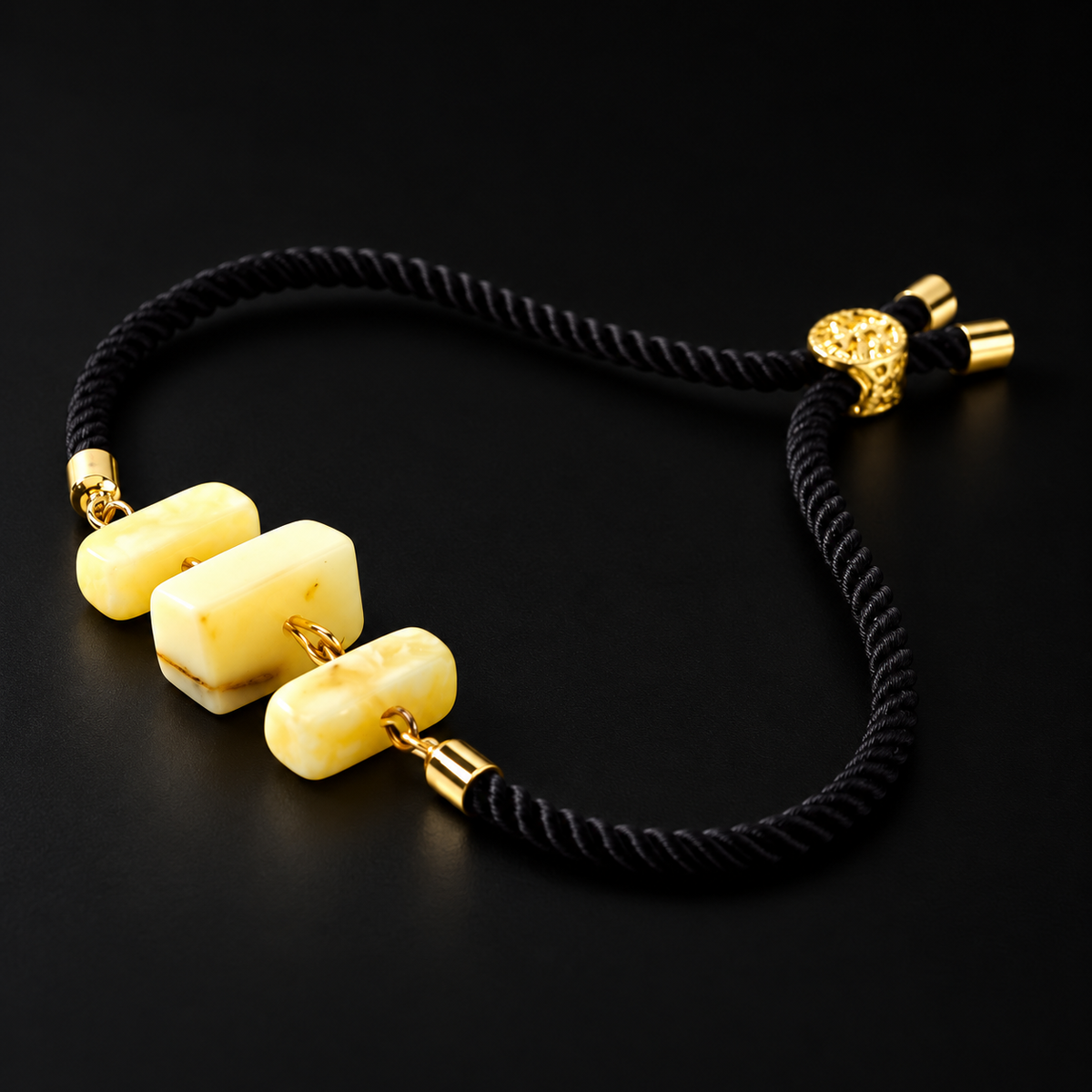 KIZIMA 3P0450q4.75 bracelet with three cream amber blocks and black cord on a black studio surface