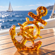 KIZIMA Baltic amber anchor on a teak yacht table with blue sea and a sailboat in the background.