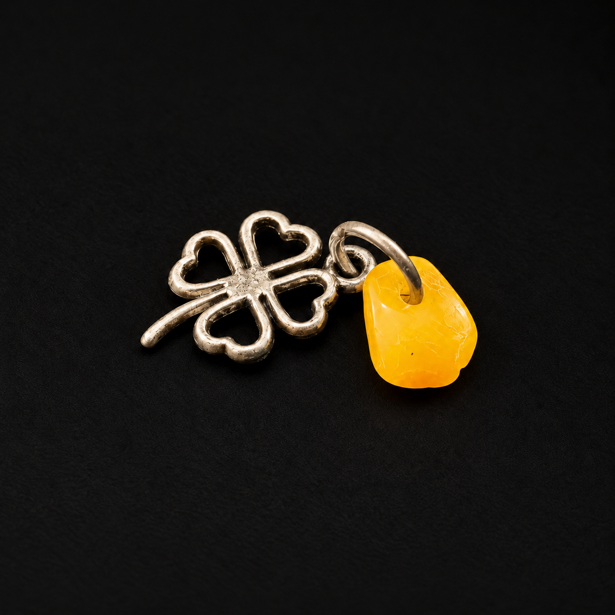 KIZIMA metal clover and natural yellow amber amulet in black studio lighting