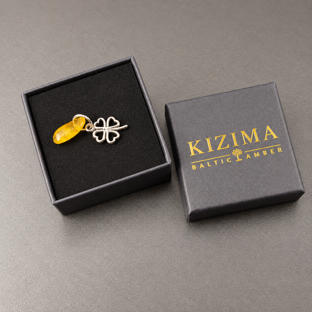 KIZIMA four-leaf metal clover amulet with natural amber displayed in its branded gift box