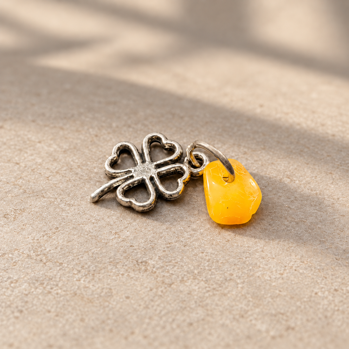 Standalone metal clover charm with natural yellow Baltic amber on a neutral tabletop