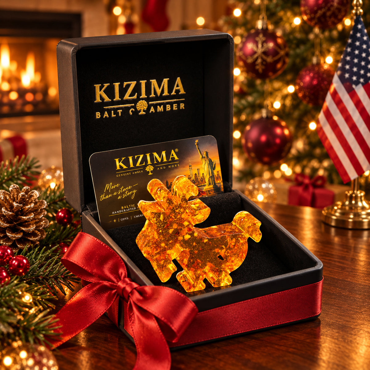 Small flat amber goat with curved horns and a beard displayed in a black KIZIMA gift box with a red satin bow, beside Christmas lights and an American flag.