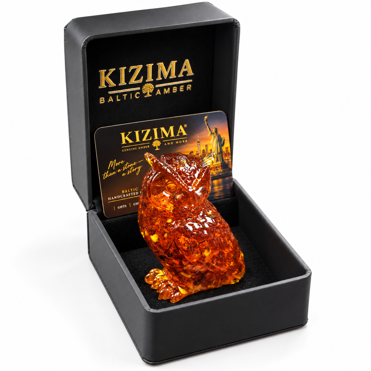 Cognac amber owl nestled in an open black KIZIMA gift box with gold branding and a New York-themed card, photographed on white.