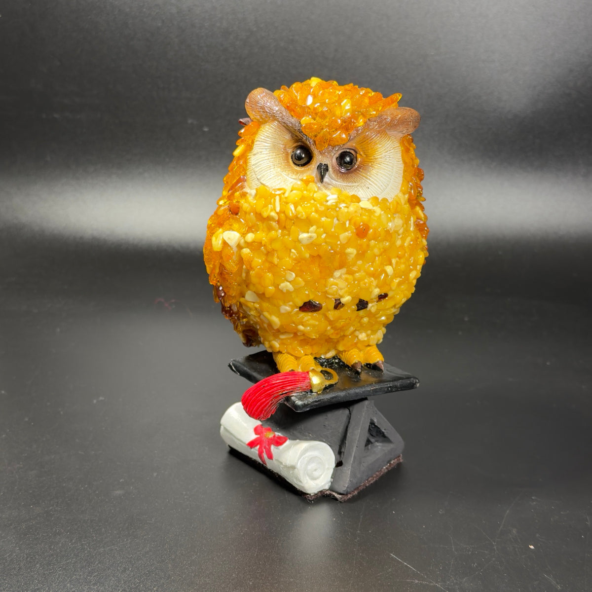 Near-front view of the handmade Brooklyn amber owl with a red diploma ribbon and red graduation tassel.