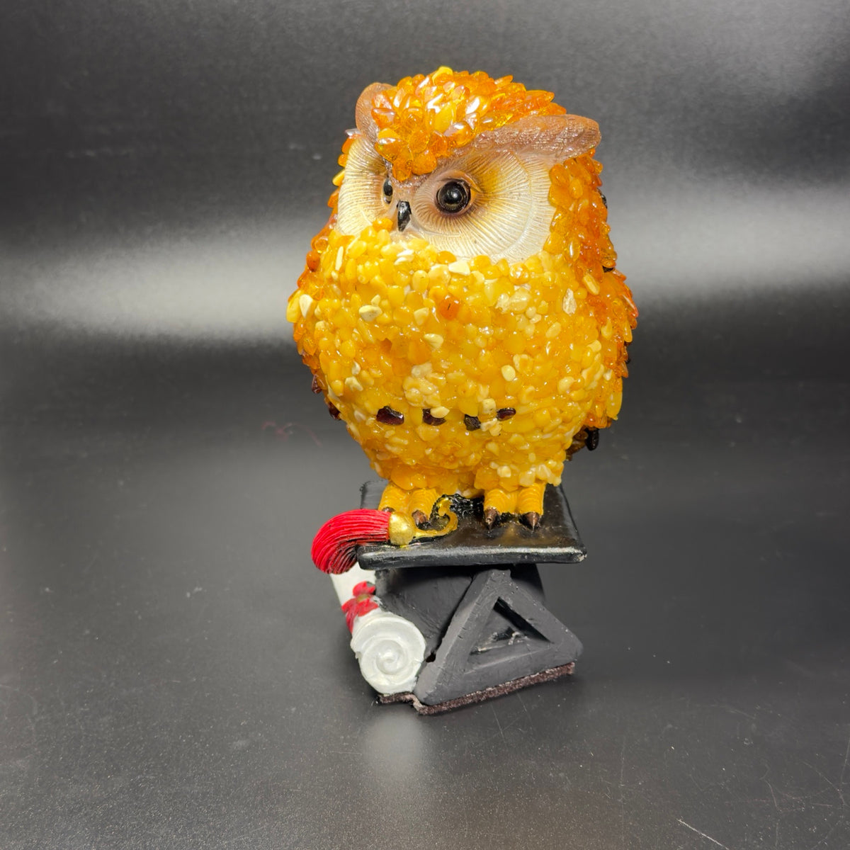 Angled close-up of the amber mosaic owl's cream face and the triangular graduation-cap base.