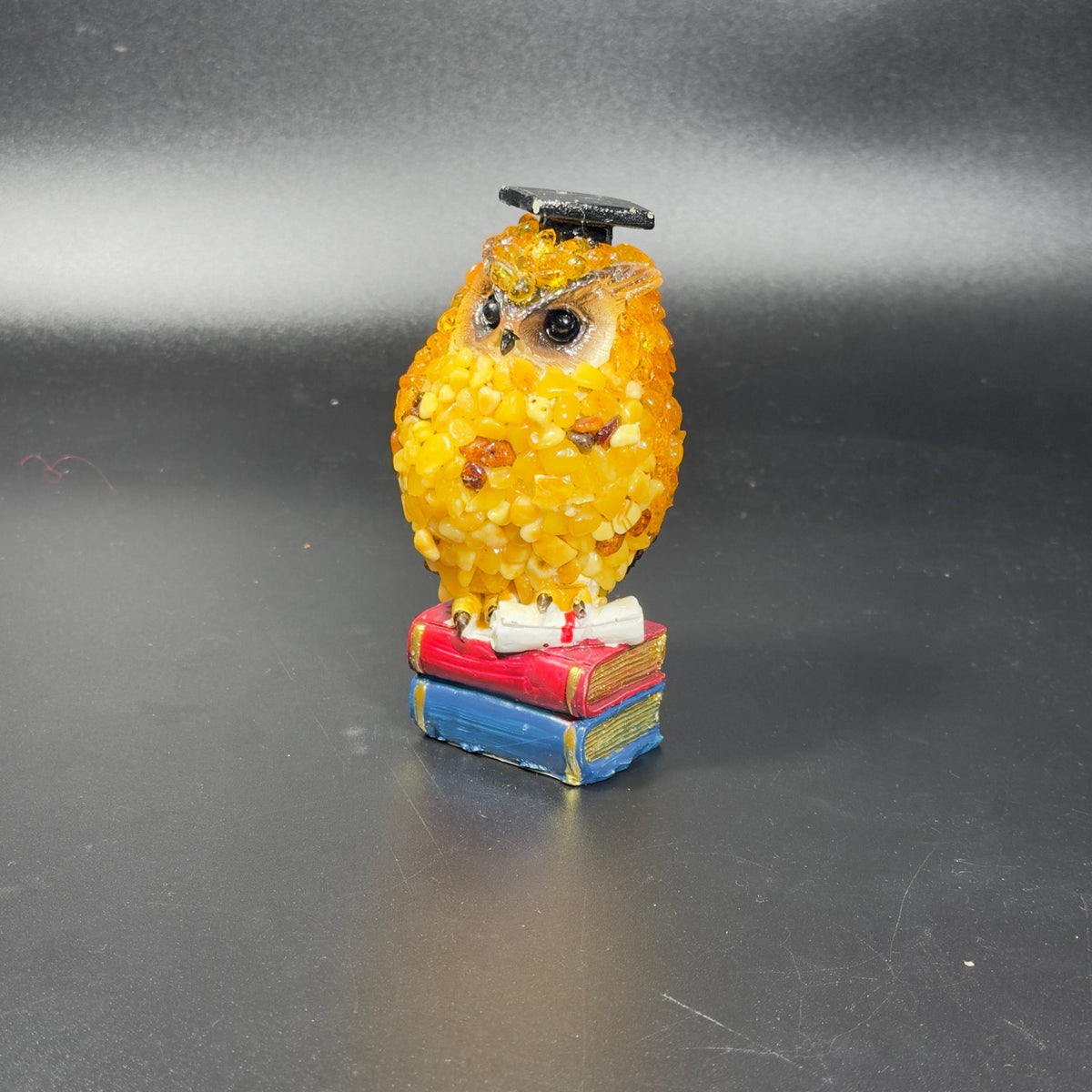 Photo of the yellow amber scholar owl in a graduation cap standing on stacked red and blue books.
