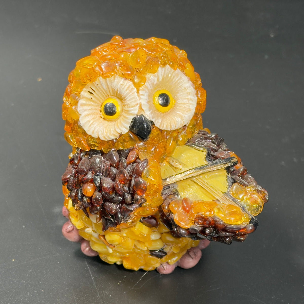 Front view of the amber owl holding a yellow violin under its chin, cream face and yellow eyes.