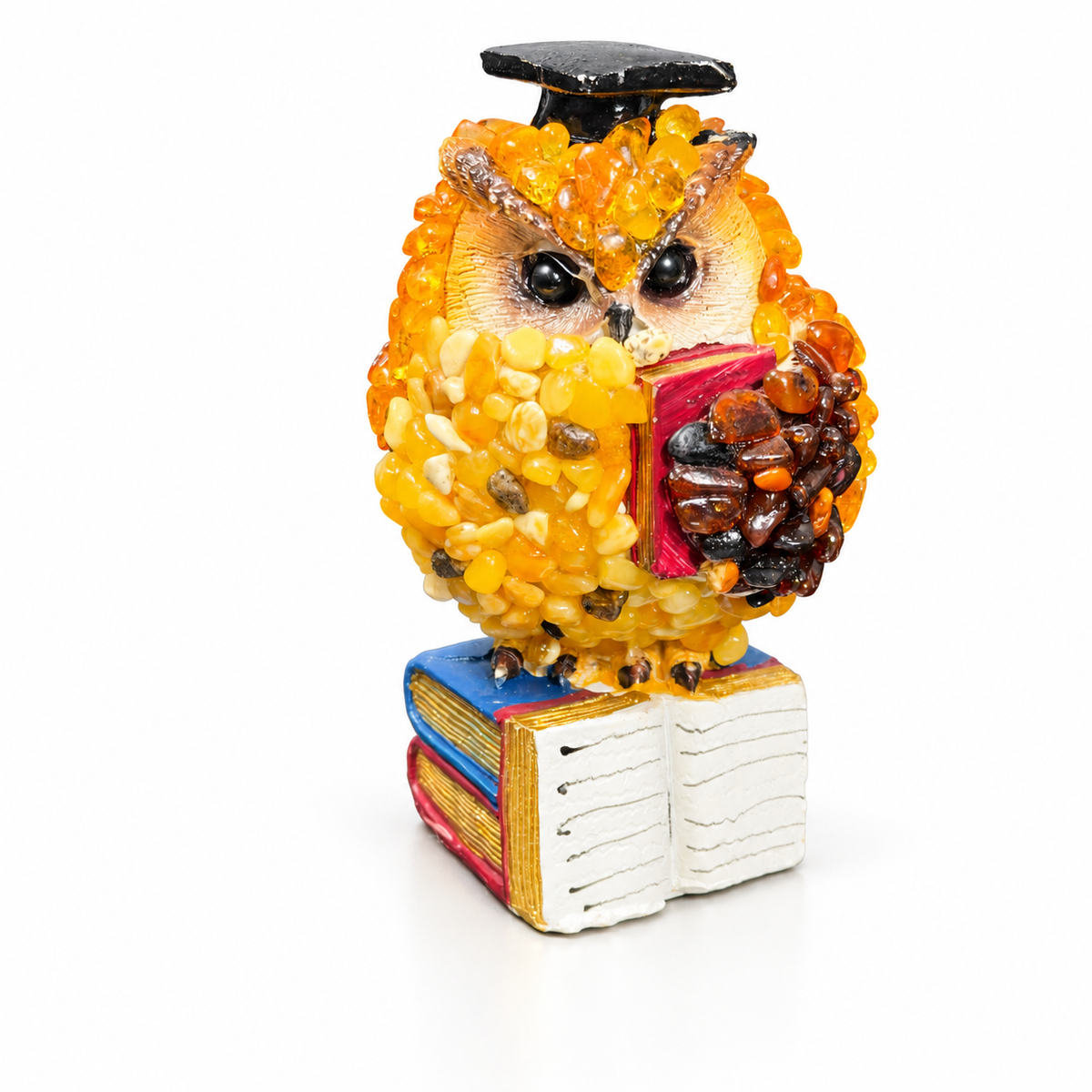 Handmade Baltic amber scholar owl holding a red book above a stack of books on a white background.