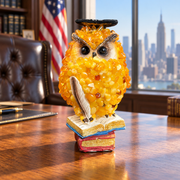 Made in USA natural Baltic amber scholar owl with a graduation cap and feather quill on books, on an oak desk in a Manhattan office.