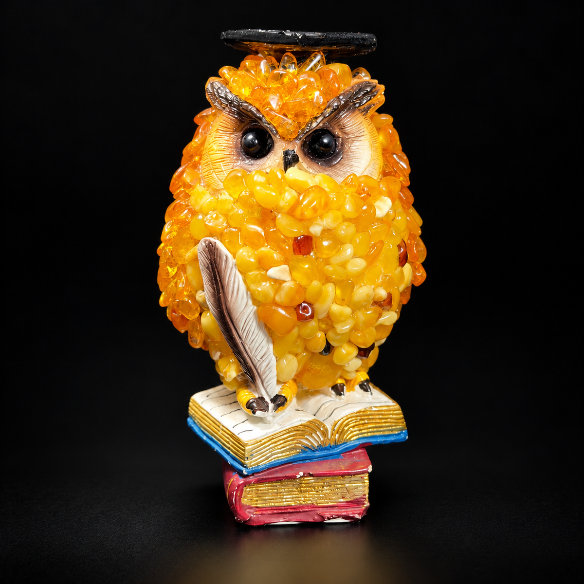 Front view of golden-yellow owl figurine holding a feather quill above blue and red books on a black background, SKU 49OWL07Q116-11-7-7