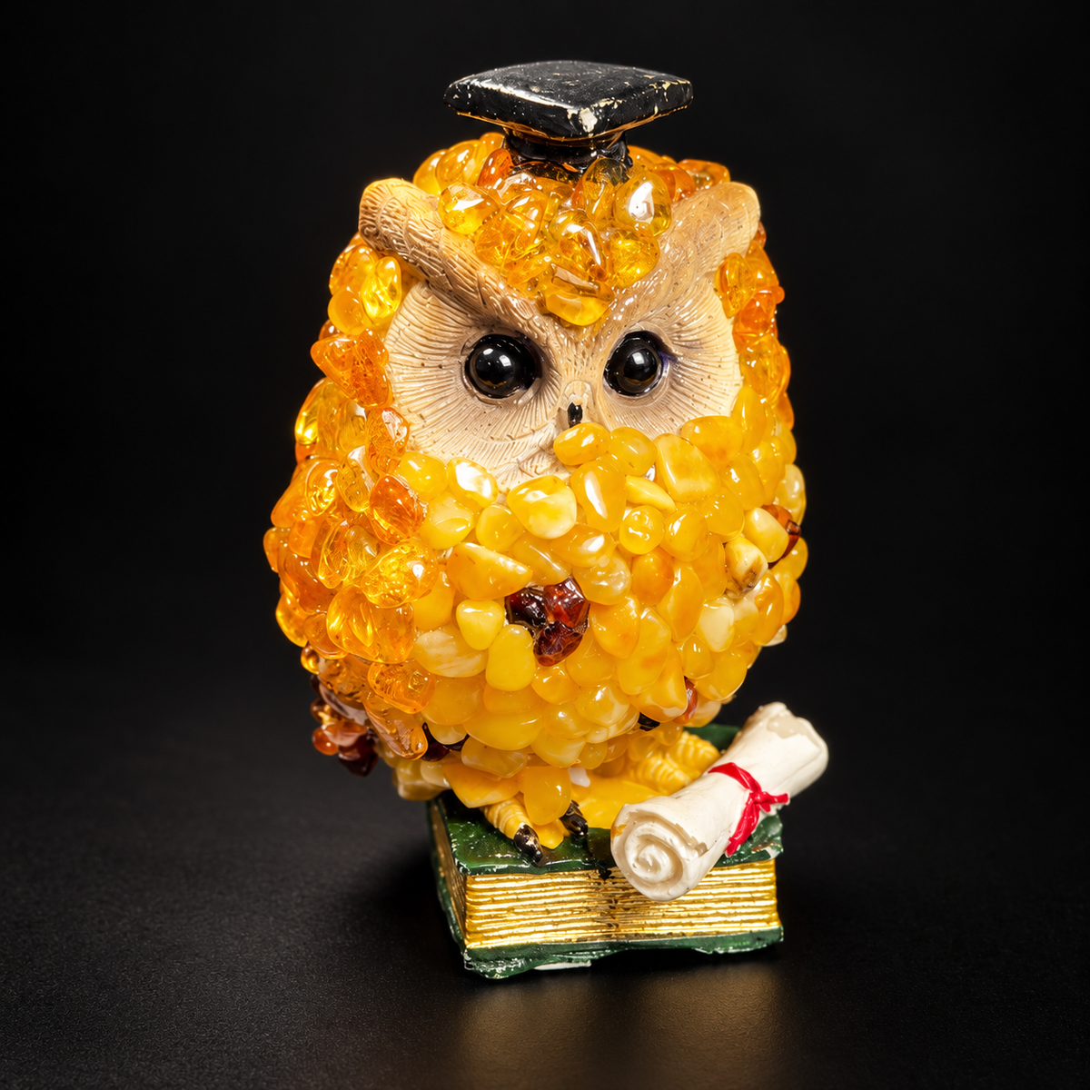 Cream-faced golden-yellow graduate owl with black mortarboard and green book against a black background