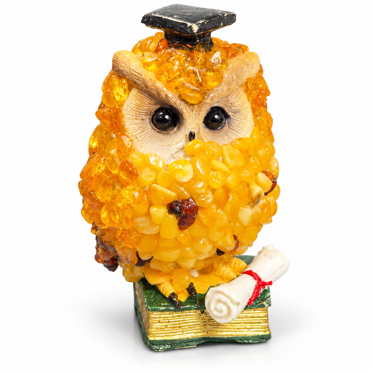 Front view of golden-yellow owl ornament on a green book with white diploma against a white background