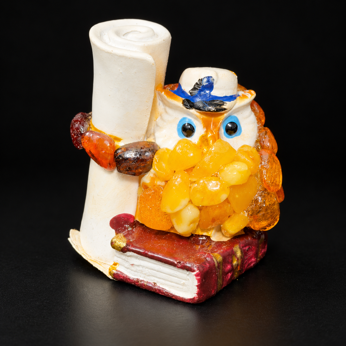 Owl figurine with blue eyes, cream hat, scroll and burgundy book on black