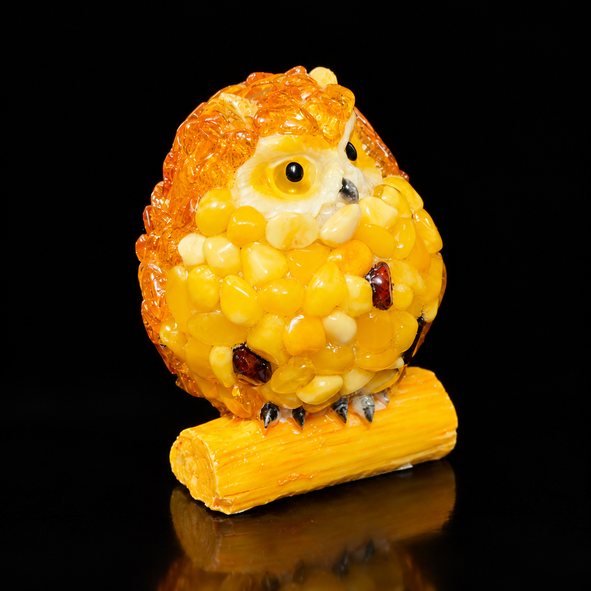 Yellow owl figurine with cream face and dark accent chips against a black studio background