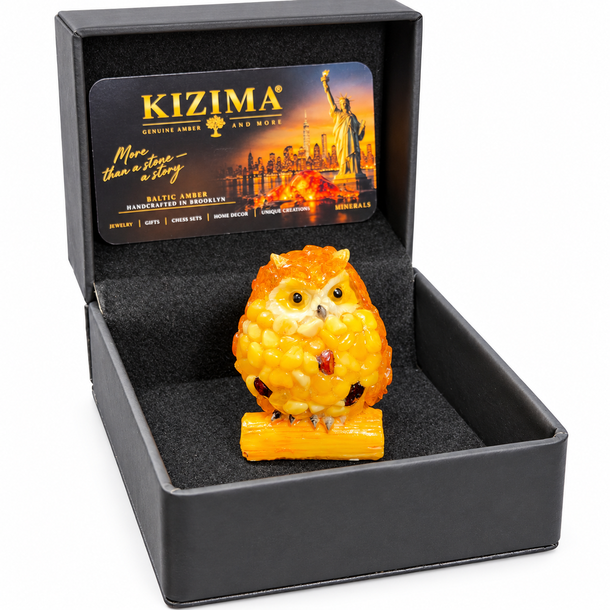 Yellow owl figurine inside its open black KIZIMA presentation box on a white background