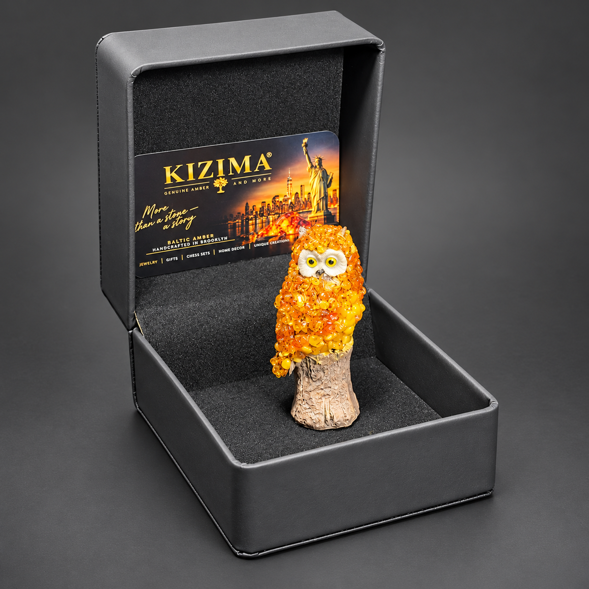 Baltic amber owl on a tree stump in its open black KIZIMA gift box with branded card, ready to give