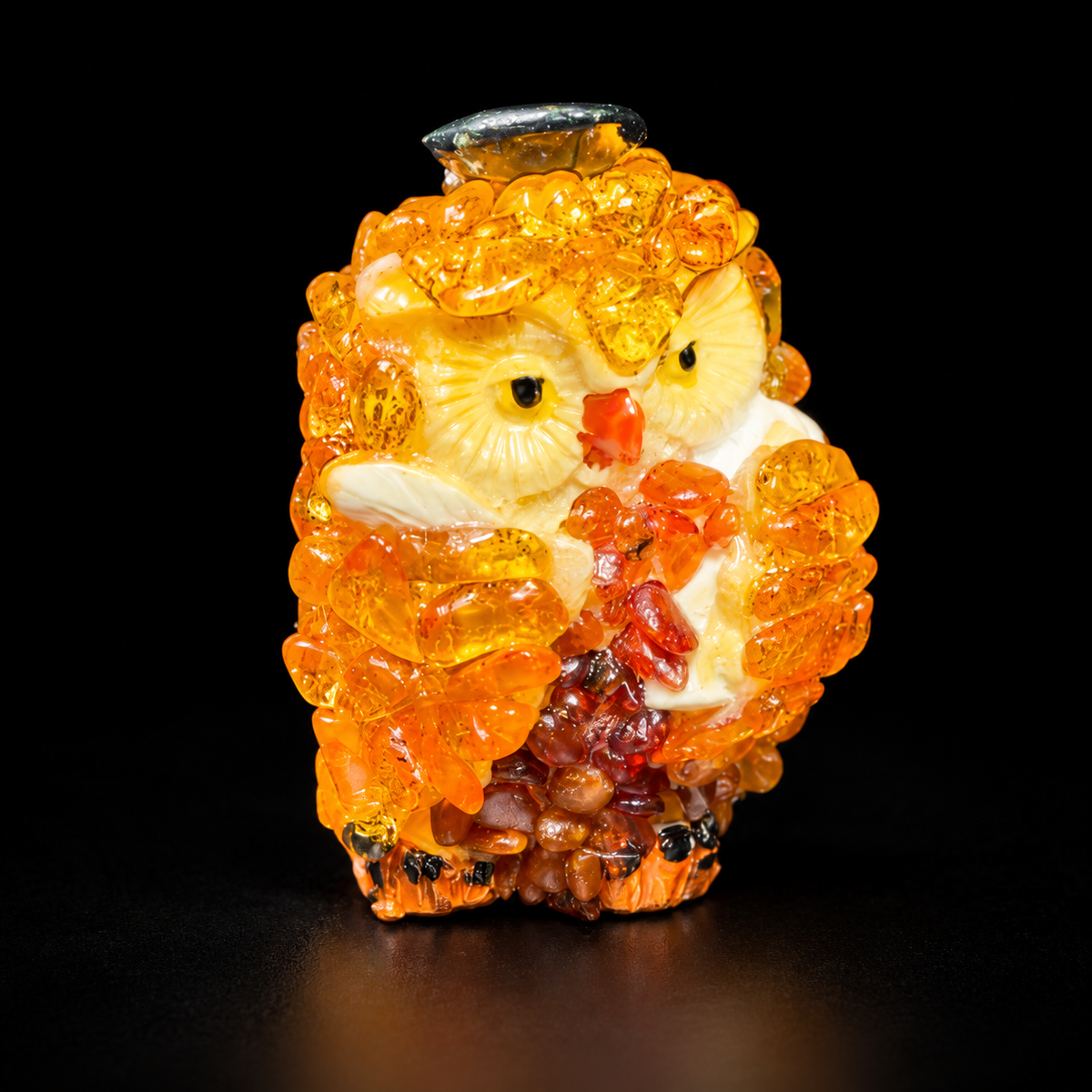 Golden-orange owl figurine with cream face and dark cap on black studio background