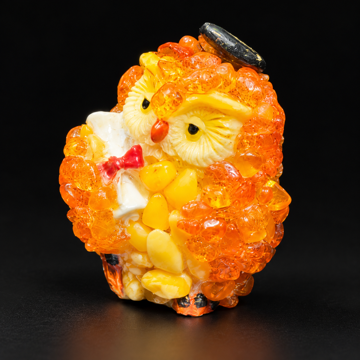 Orange graduation owl figurine holding a diploma against a black studio background
