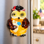 Made in USA natural Baltic amber graduation owl fridge magnet on a stainless steel refrigerator in a bright kitchen.