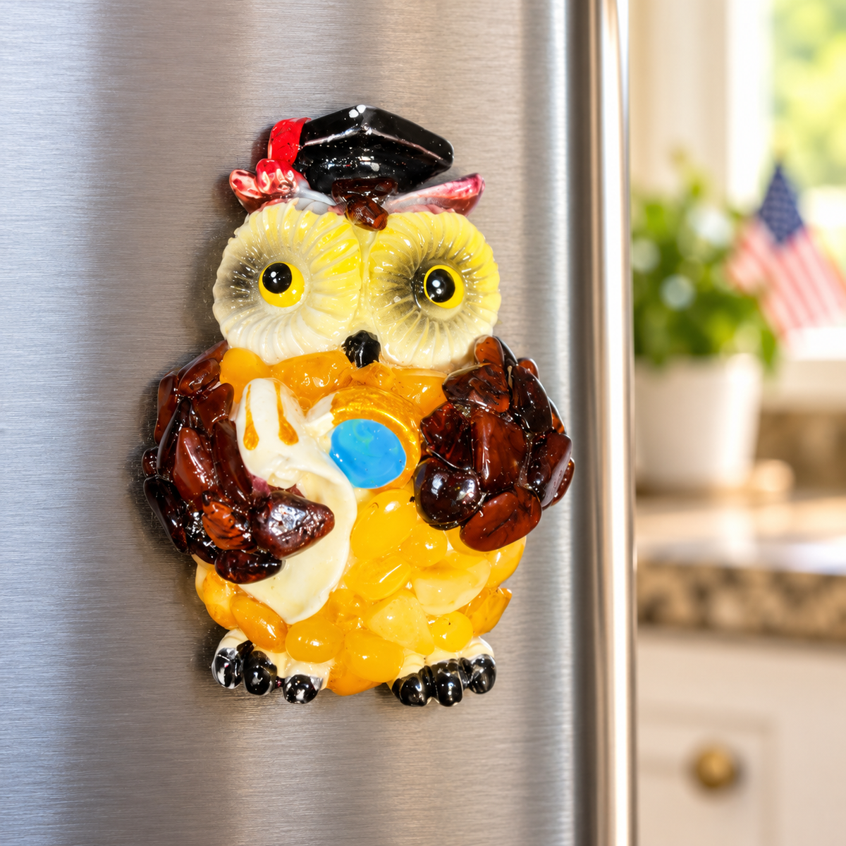 Made in USA natural Baltic amber graduation owl fridge magnet on a stainless steel refrigerator in a bright kitchen.