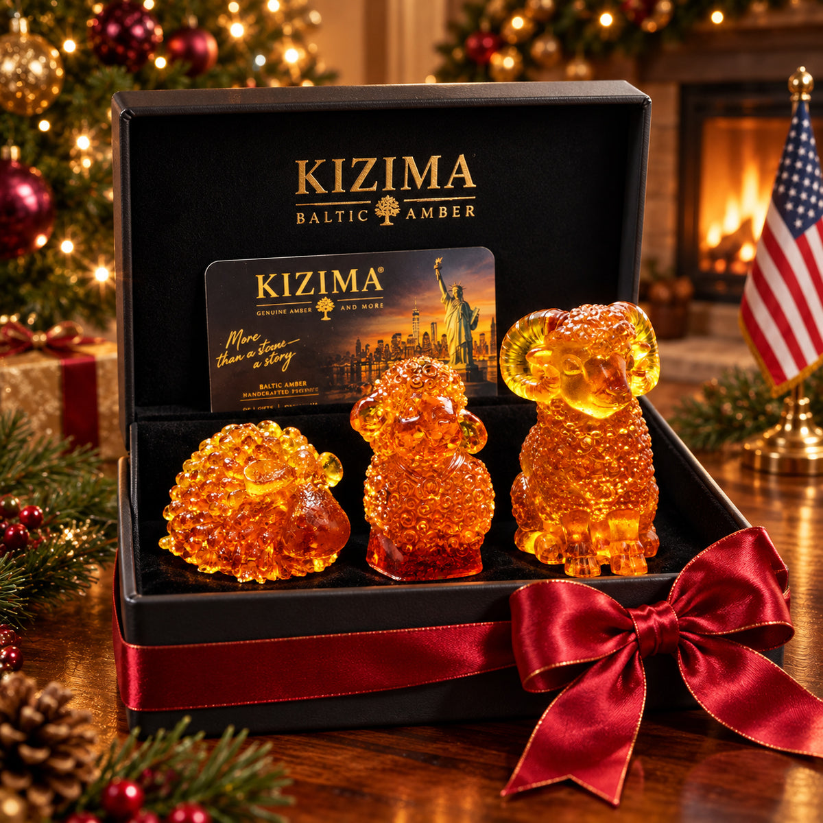 Three distinct amber sheep and ram figurines arranged from shortest to tallest inside a black KIZIMA box with red satin ribbon, against a Christmas tree, fireplace and American flag.