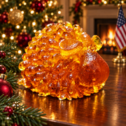 Compact golden amber sheep with small ears and a rounded nose on a walnut table, with a decorated Christmas tree, fireplace and American flag.
